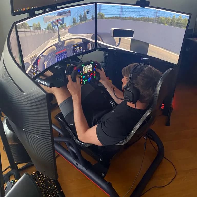 Max Verstappen at a racing simulator, holding the steering wheel in front of multiple monitors