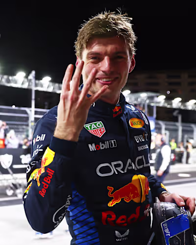 Max Verstappen smiling and raising four fingers, with his face, torso and hand visible